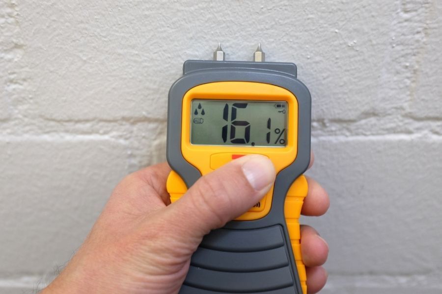Restoration technician taking a moisture meter reading on a drywall surface