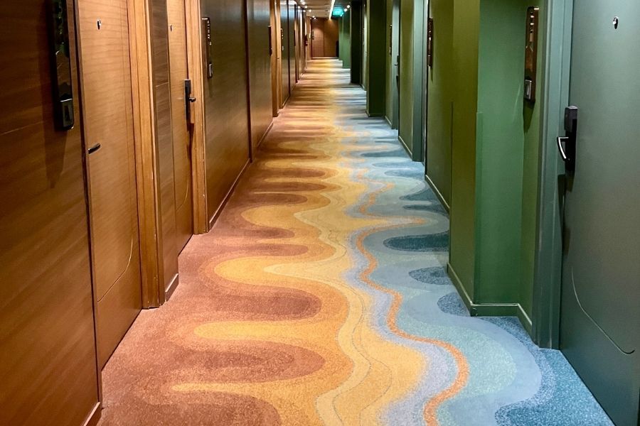 Long hallway lined with guest room doors and patterned carpet running the length of the corridor