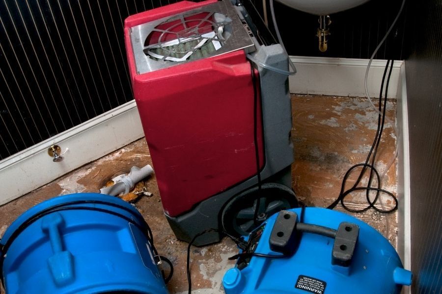 Extraction machine and air movers set up on a stained bathroom floor during sewage cleanup in Largo FL