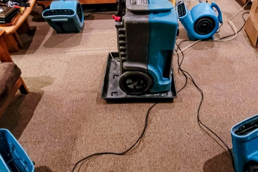 Row of professional air movers drying wet carpet in a Florida living room