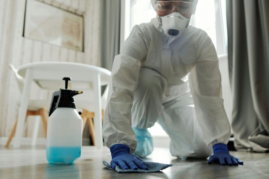 Restoration technician in protective suit and gloves sanitizing a floor after sewage cleanup in Largo, FL