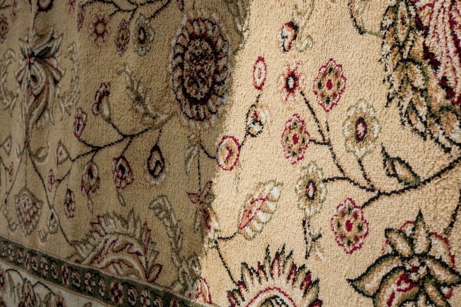 Close-up of a patterned area rug showing a brighter cleaned section beside the untouched side