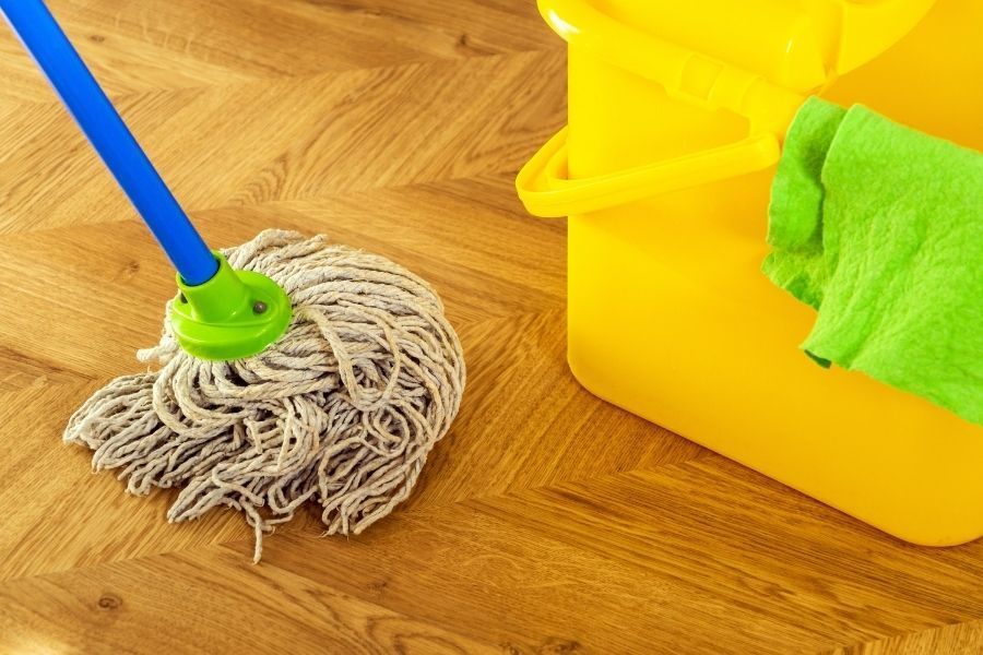 Cotton mop and yellow cleaning bucket on a wood floor during water cleanup