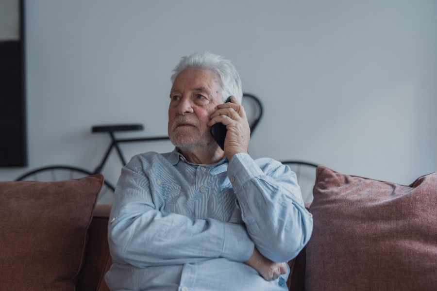 Older man sitting on a couch making a phone call after discovering water damage at home