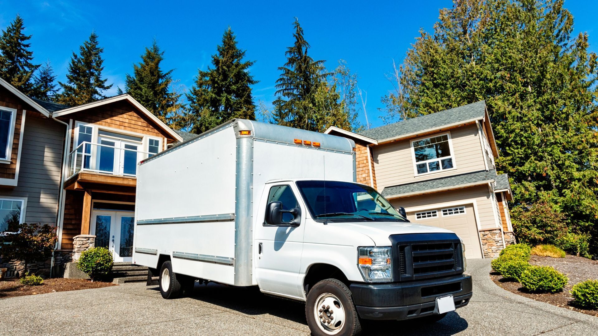 White box truck parked in a suburban driveway in front of houses on a sunny day