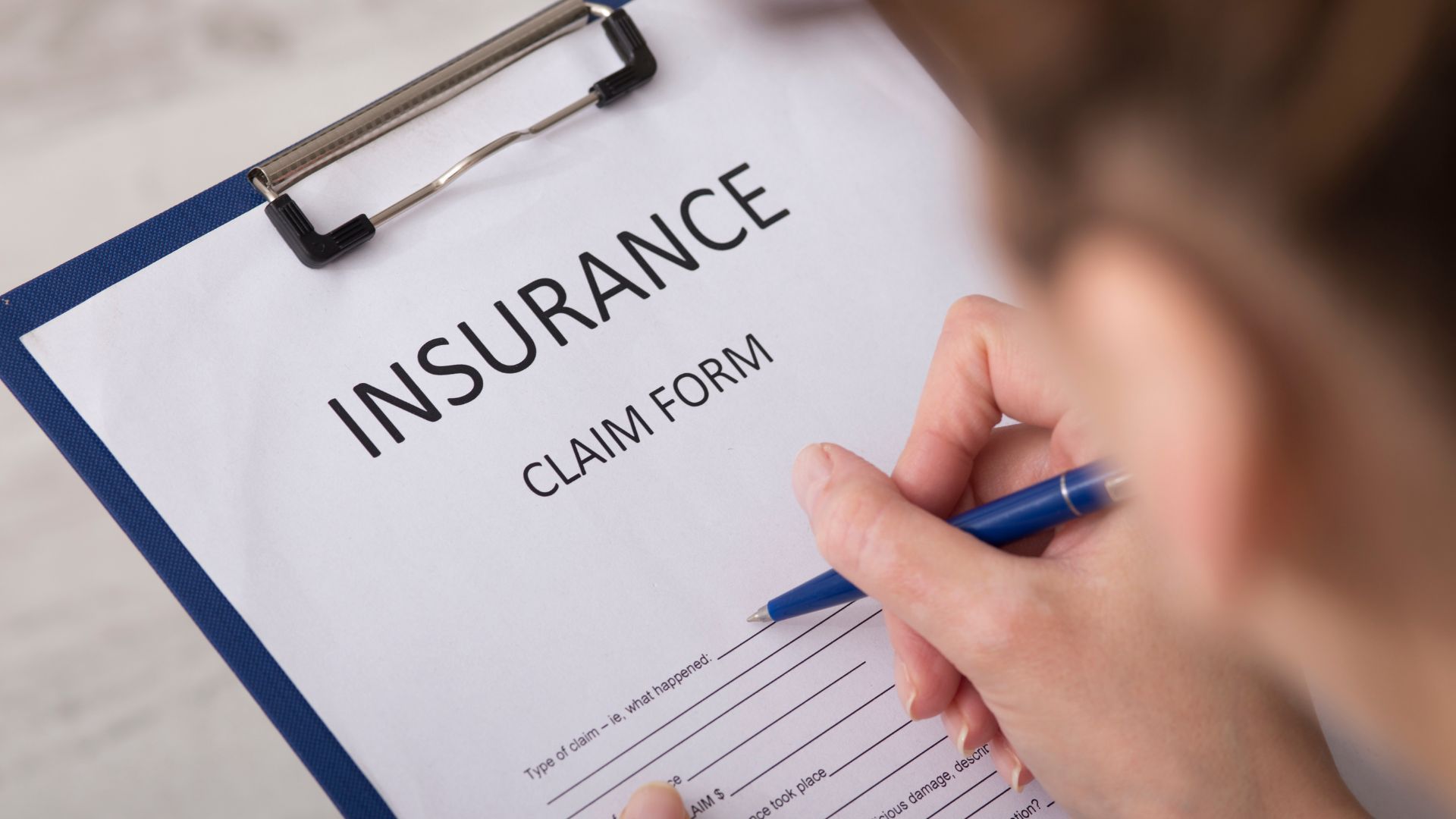 Hand writing on a clipboard insurance claim form with a blue pen