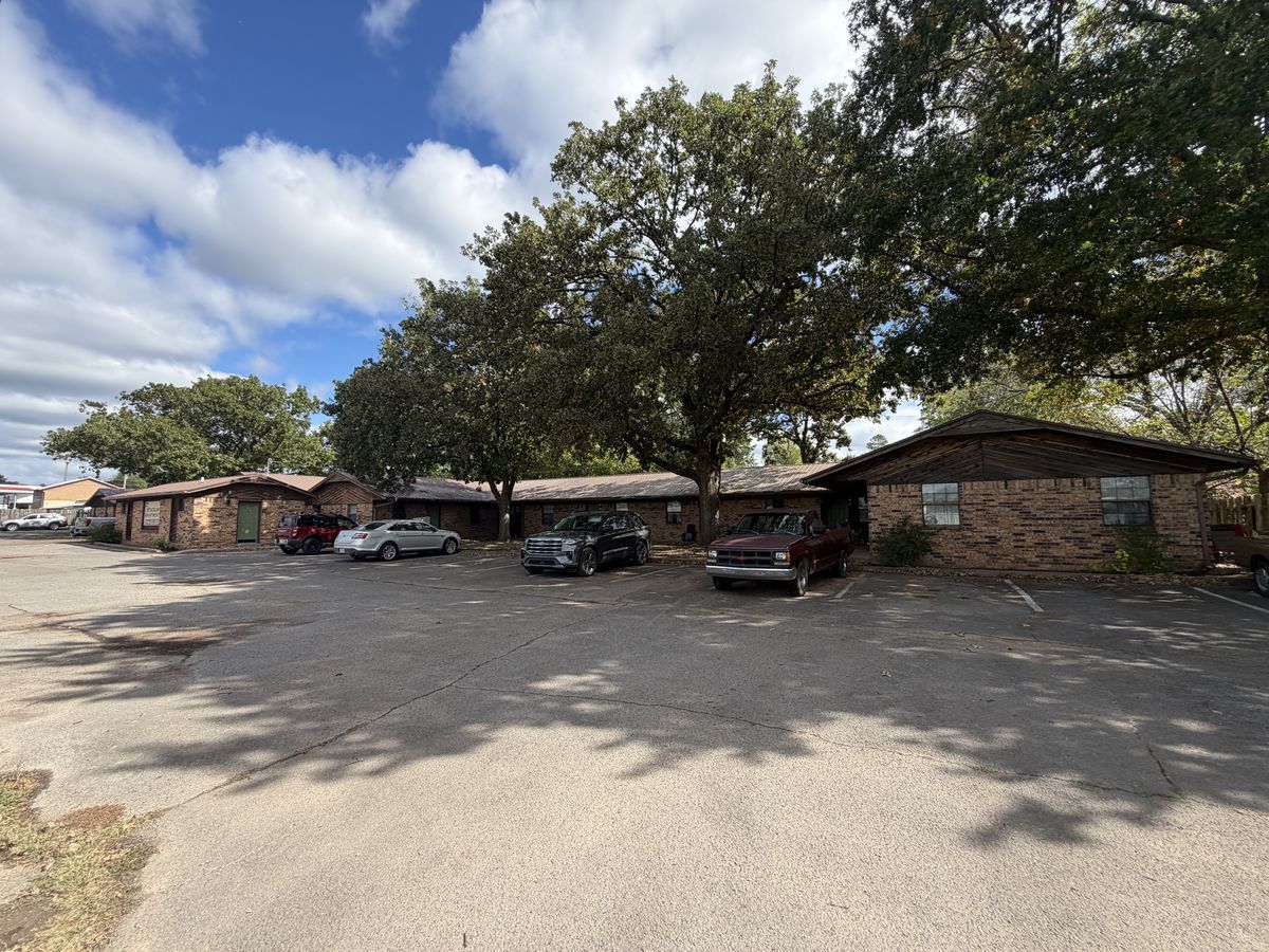 Single-story brick apartments shaded by large oak trees at Stadium Apartments