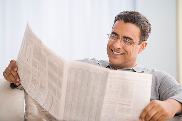 a man is sitting on a couch reading a newspaper .