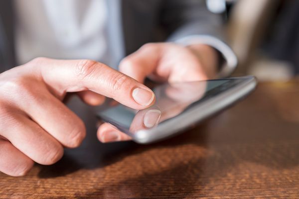 a man is sitting at a table using a cell phone .