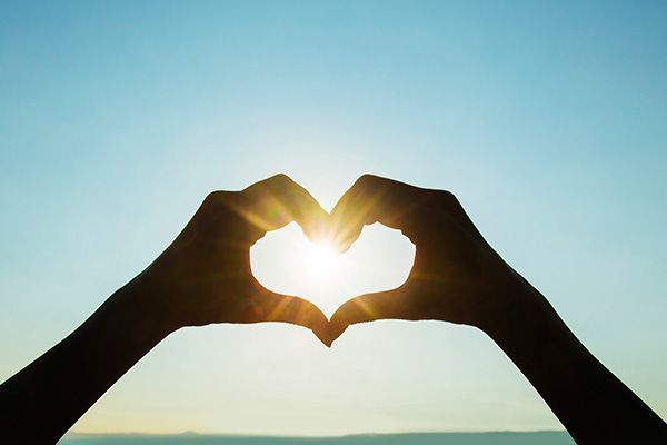 a person is making a heart shape with their hands in front of the sun .