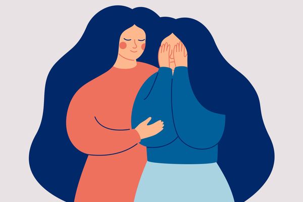 a woman is hugging another woman who is covering her face with her hands .