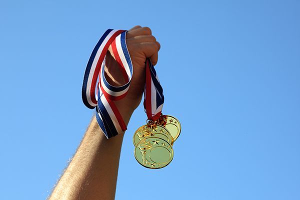 a person is holding three gold medals in their hand against a blue sky .