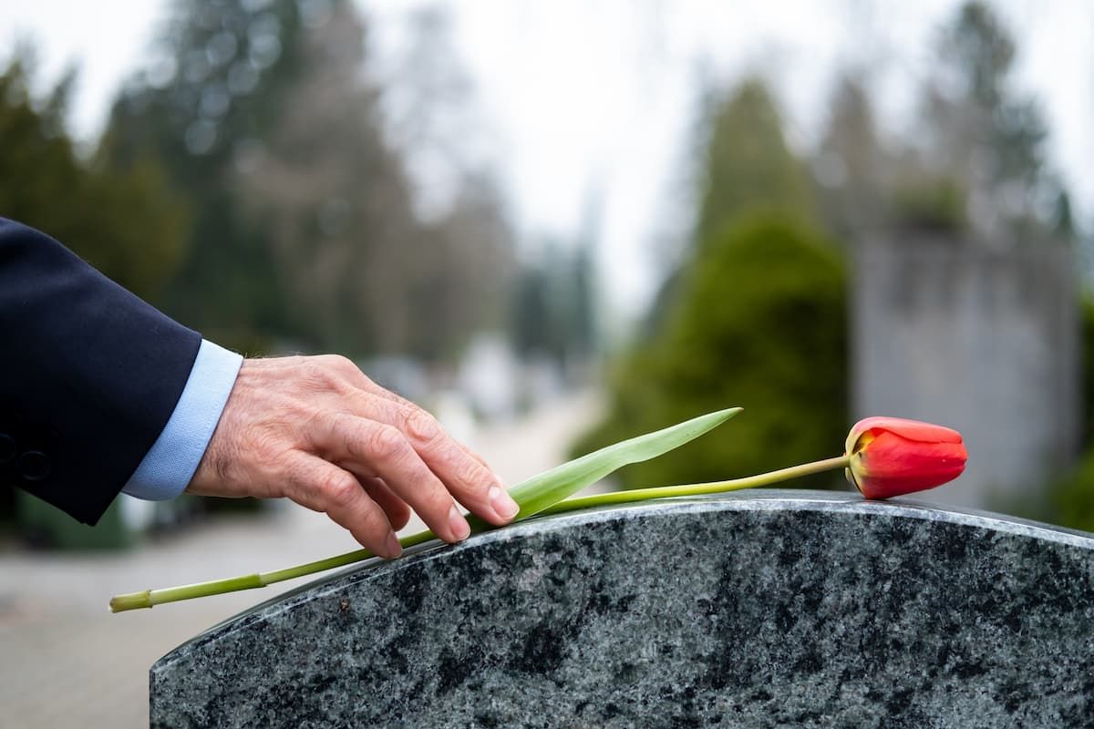 A man is putting a red tulip on a grave.