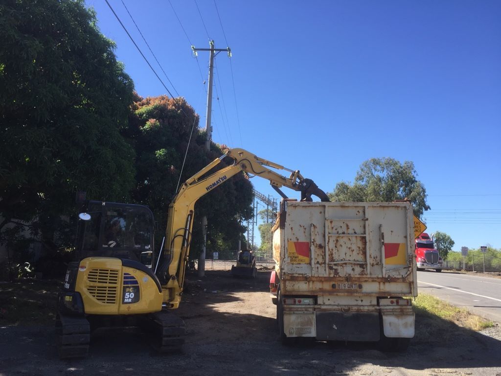 Yellow Excavator Loading Debris Into a White Truck by a Road, Under Power Lines — Huntlys Heavy Equipment in Gracemere, QLD