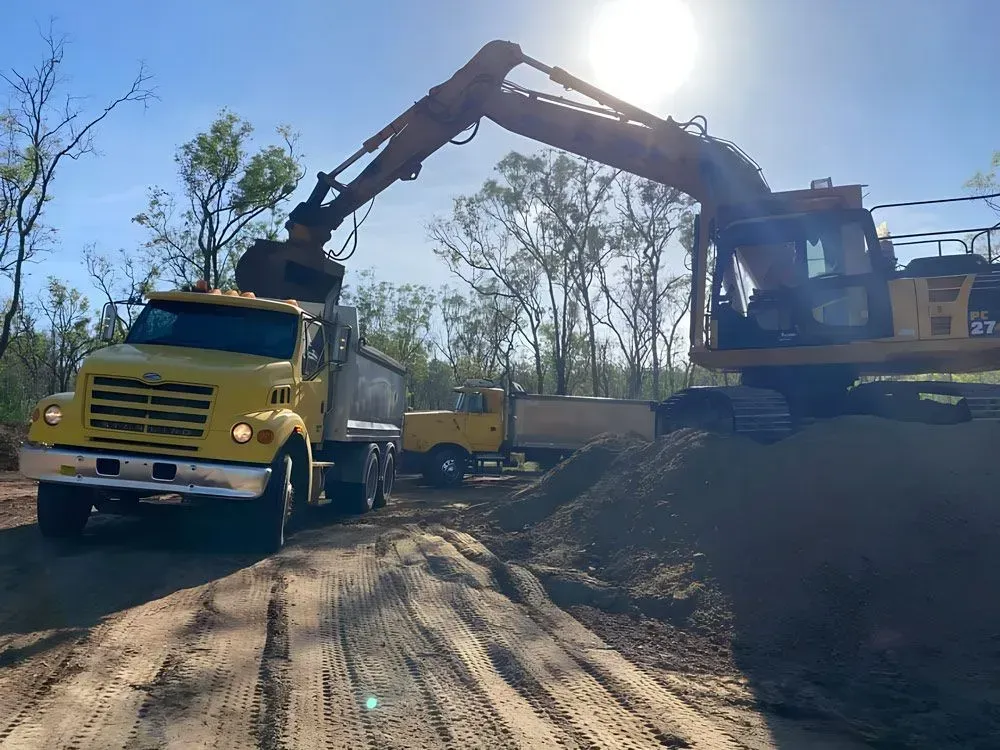 Yellow Excavator Loading a Dump Truck With Gravel on a Dirt Road — Huntlys Heavy Equipment In Gracemere, QLD