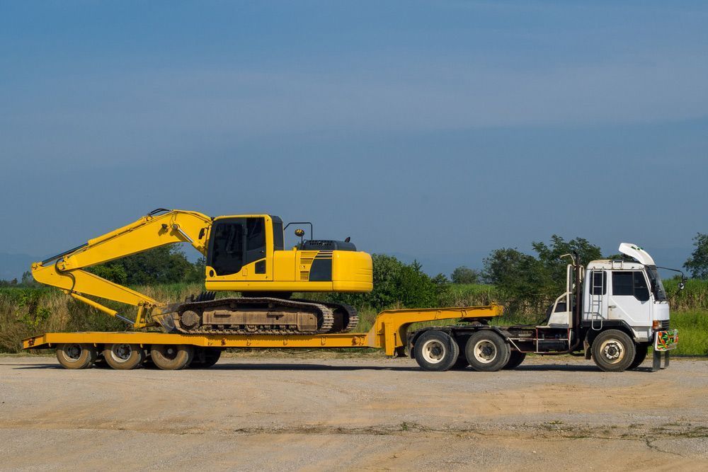 Yellow Excavator on a Flatbed Trailer Being Towed by a White Truck on a Dirt Road — Huntlys Heavy Equipment in Gracemere, QLD