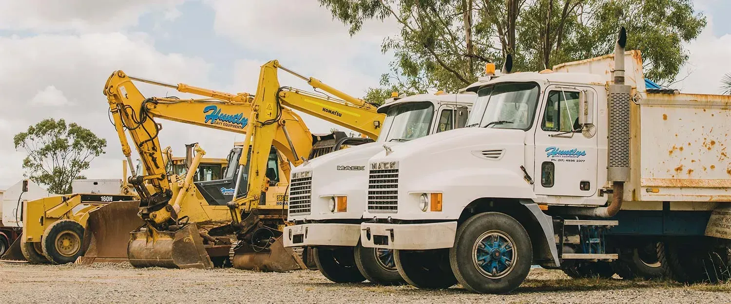 Yellow Excavator and Dump Trucks Parked Outside — Huntlys Heavy Equipment In Gracemere, QLD