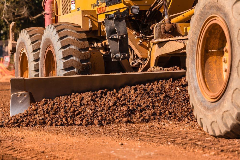 Yellow Grader Smoothing Red Dirt Road — Huntlys Heavy Equipment in Gracemere, QLD