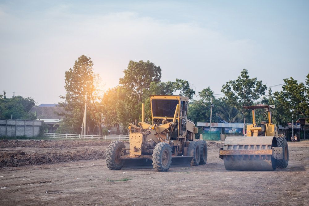 Yellow Construction Vehicles on a Dusty Lot With Trees and a Building — Huntlys Heavy Equipment in Gracemere, QLD