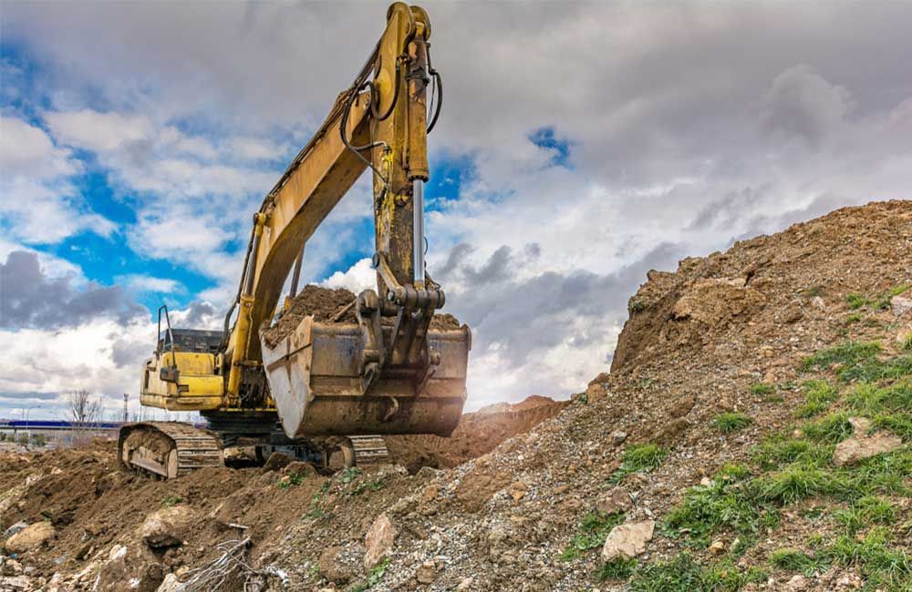 Yellow Excavator Digging Into a Pile of Dirt, Under a Cloudy Sky — Huntlys Heavy Equipment in Gracemere, QLD
