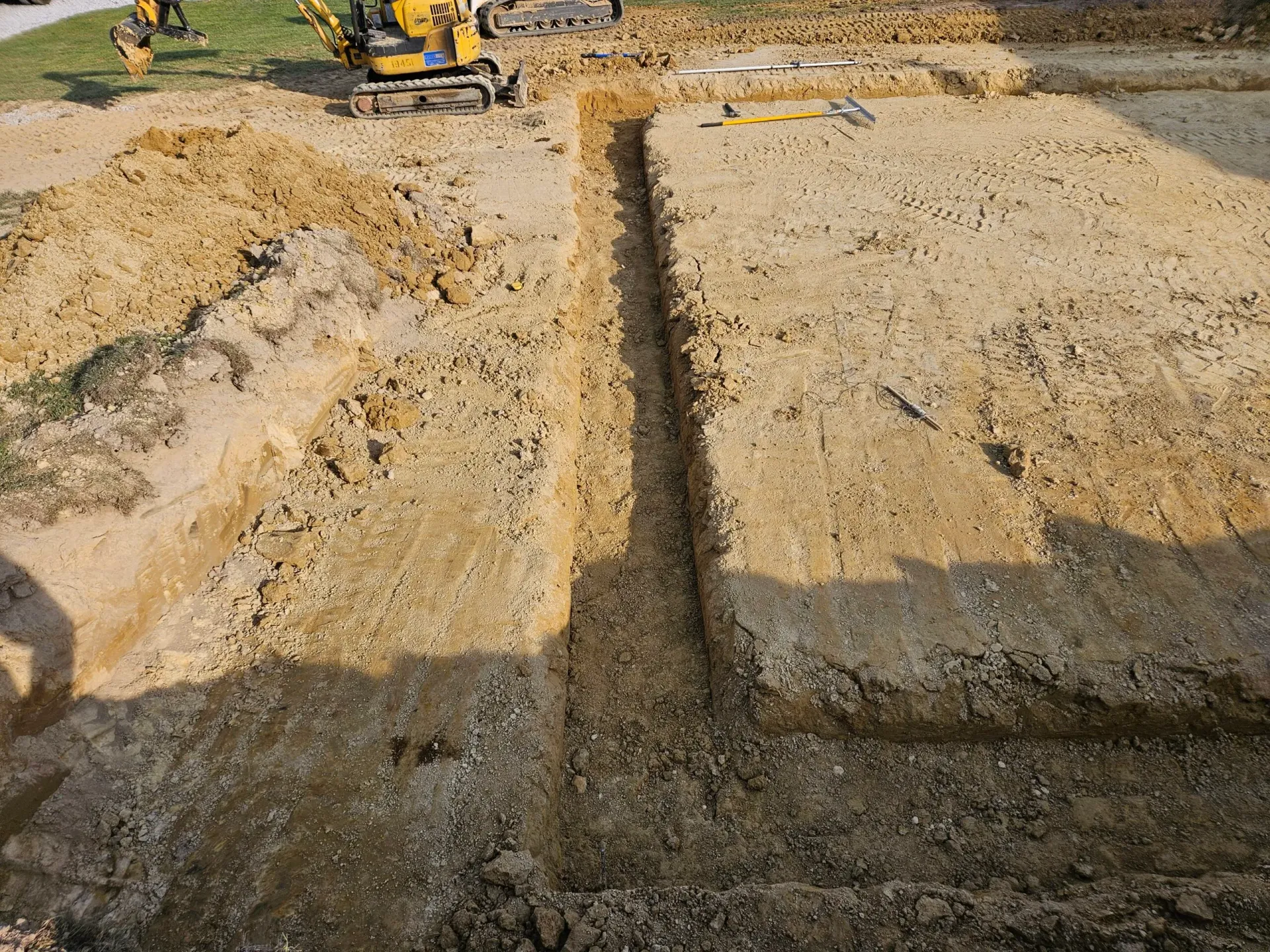 Construction site with two large dug-out trenches and an excavator in the background