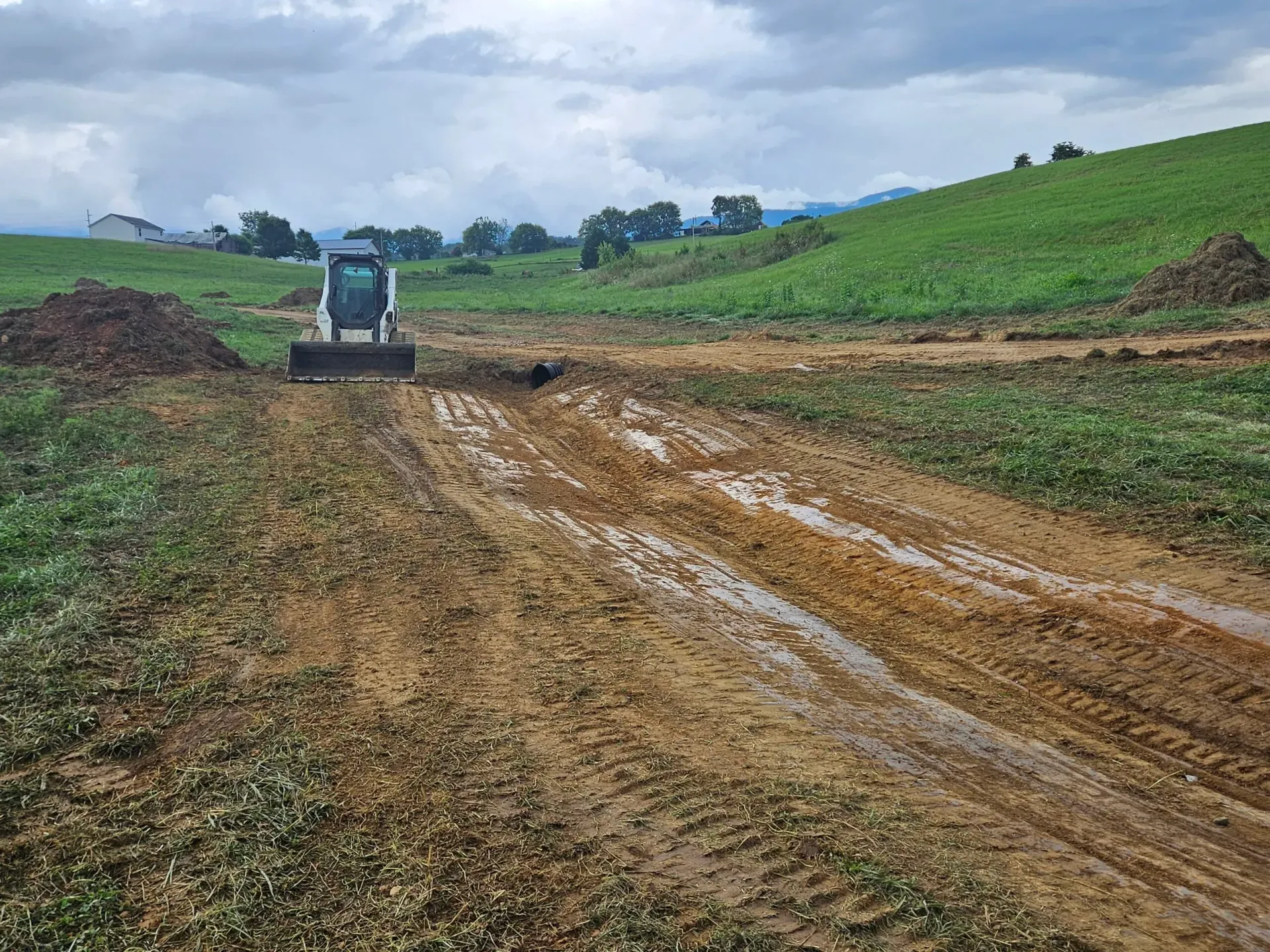 Tractor on muddy dirt road in a green сельский hillside field under cloudy sky