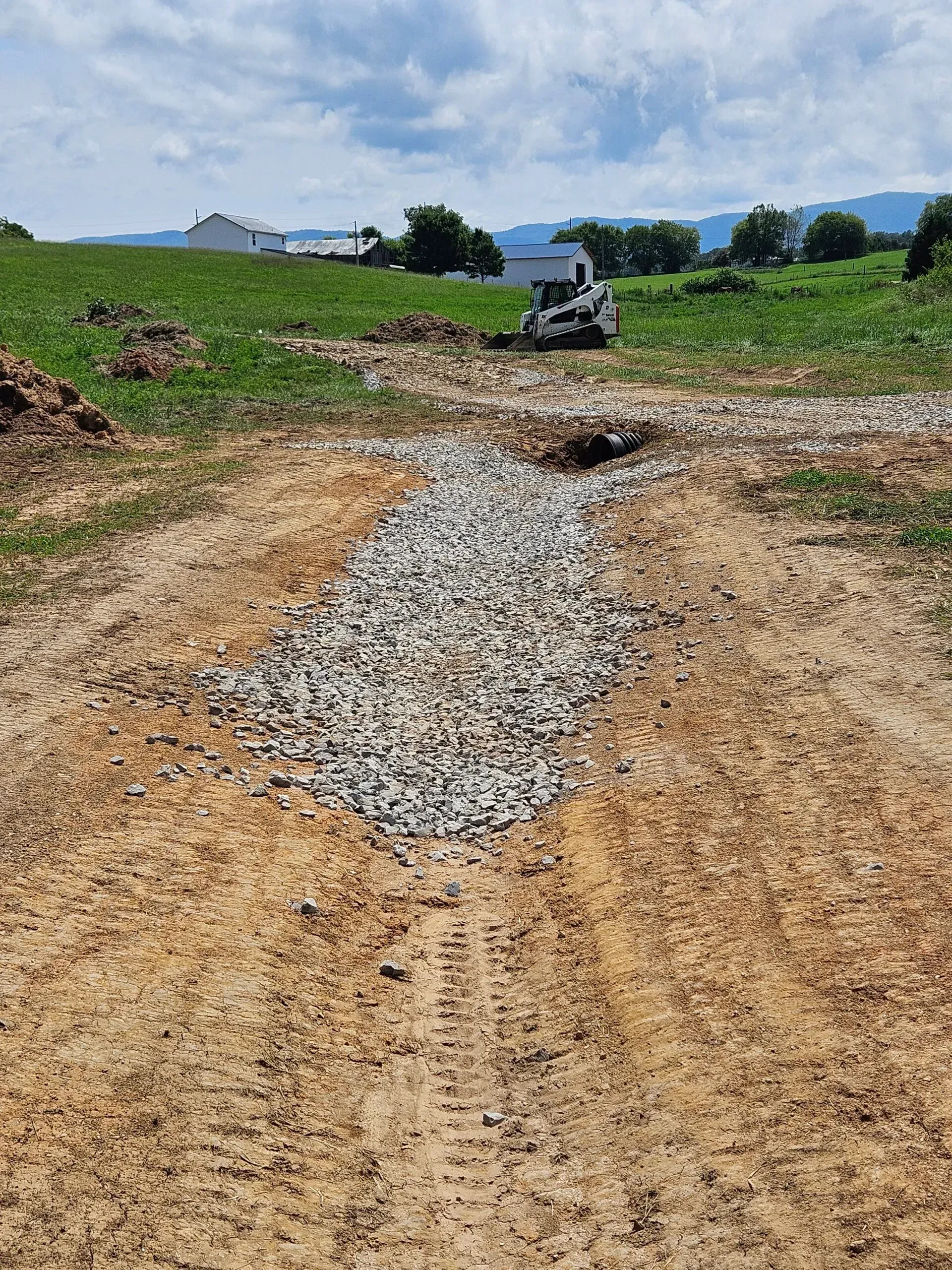 Gravel path through green field with a parked utility vehicle under a cloudy sky
