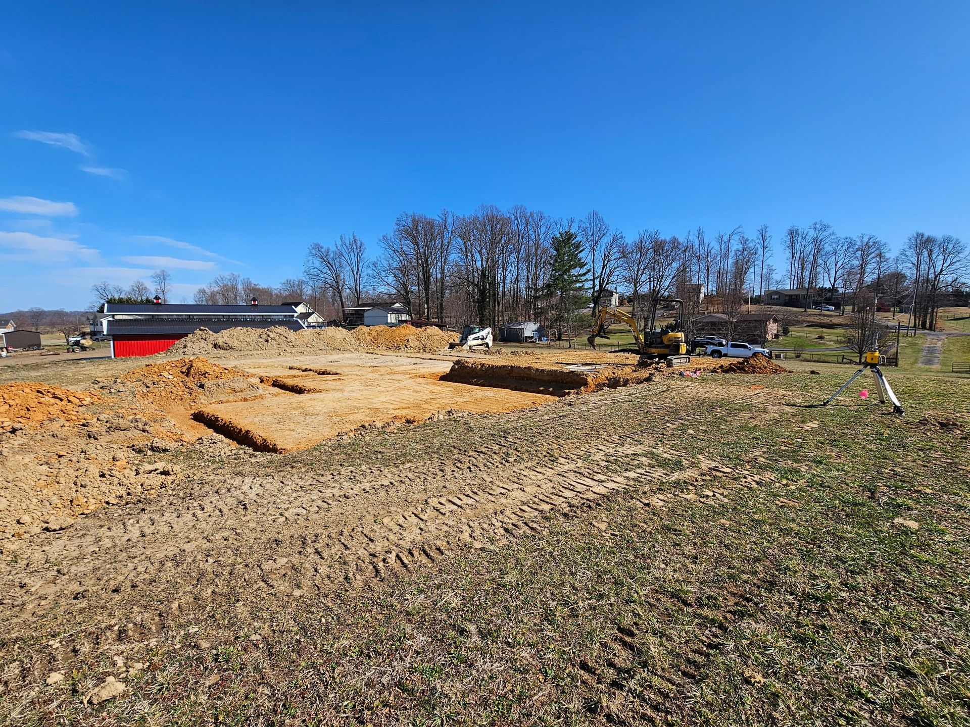 Cleared construction site with sand piles and a red building under a bright blue sky