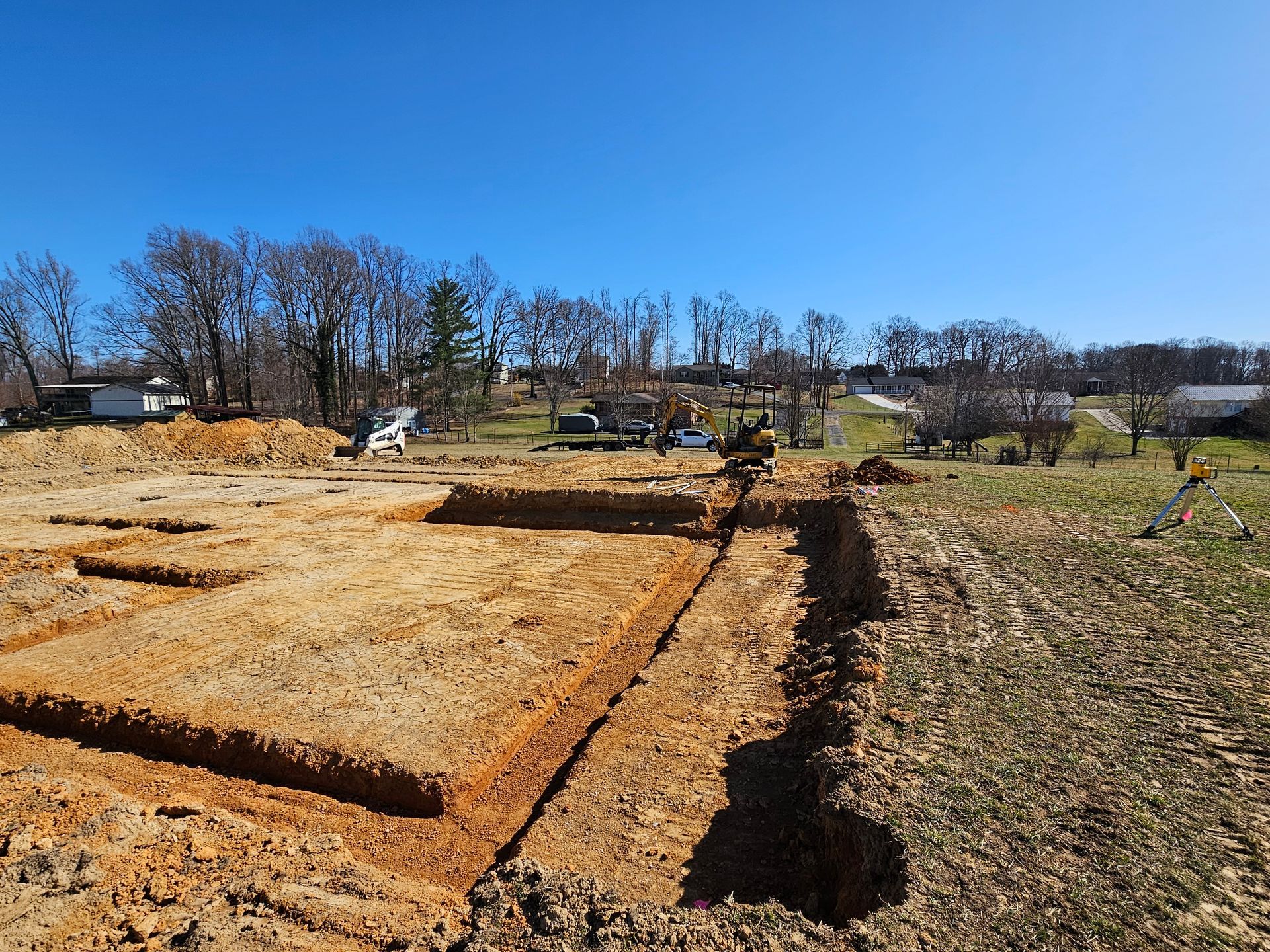 Outdoor scene with straw-covered garden plots, dirt paths, and leafless trees under a clear blue sky