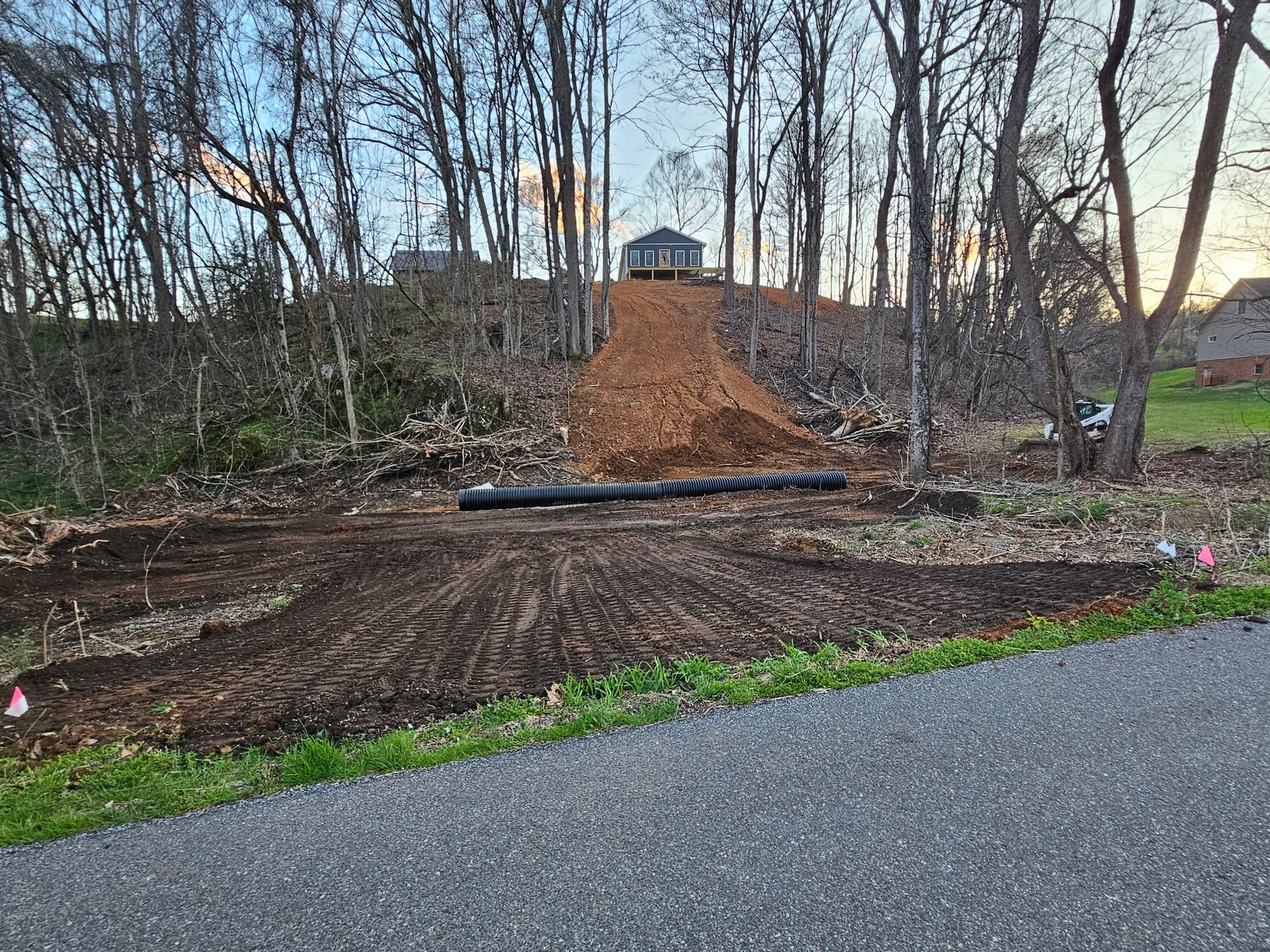 Large dirt ramp under construction in a wooded yard beside a paved road at dusk