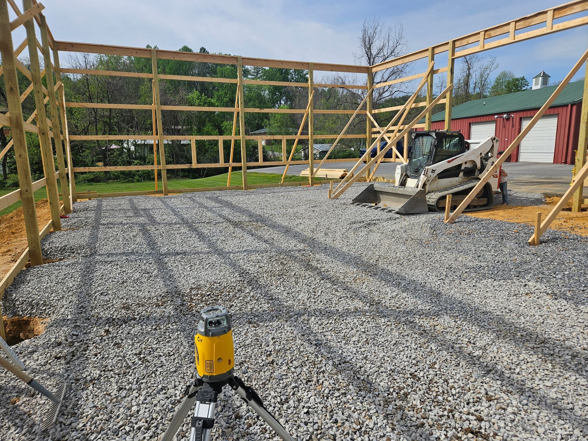 Gravel-floored construction site with wooden wall framing and a yellow work light in the foreground