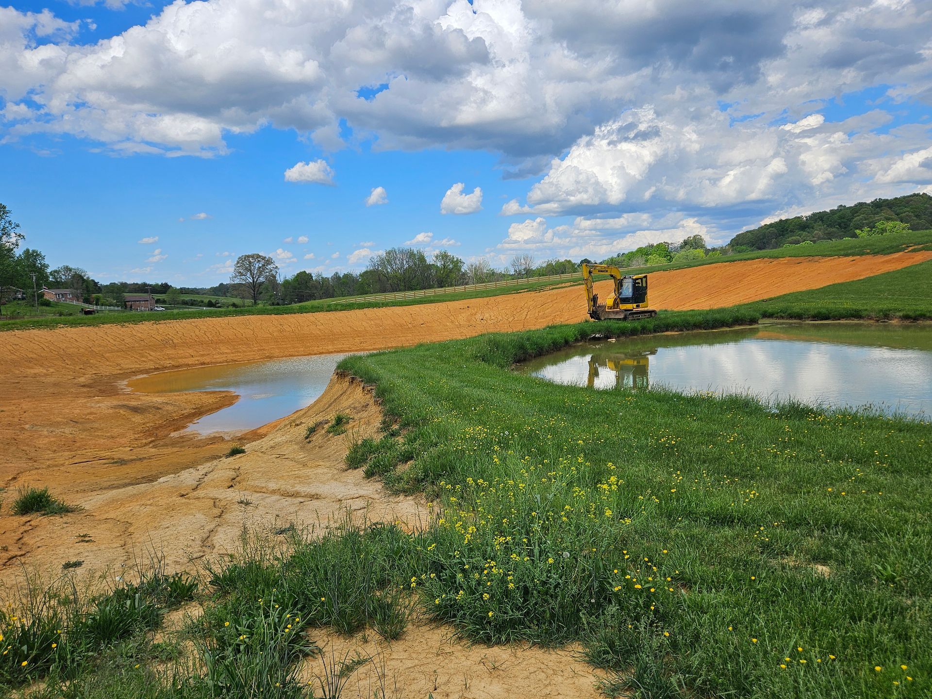 Sunny rural field with a water-filled ditch, green grass, and two tractors under a cloudy blue sky