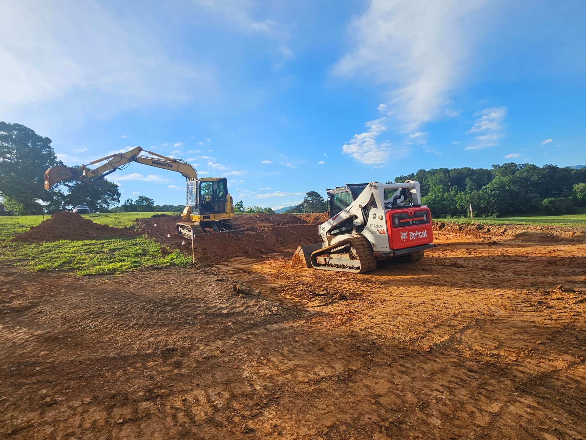 Excavator and skid steer moving dirt at a construction site under a blue sky