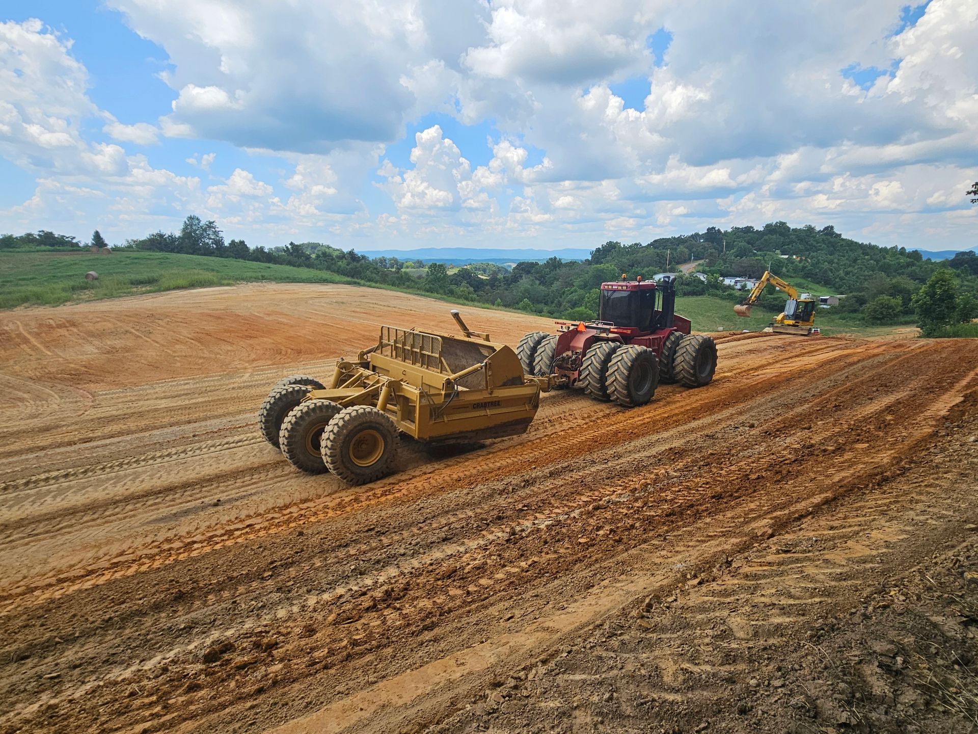 Two heavy machines grading a dirt field under a cloudy sky
