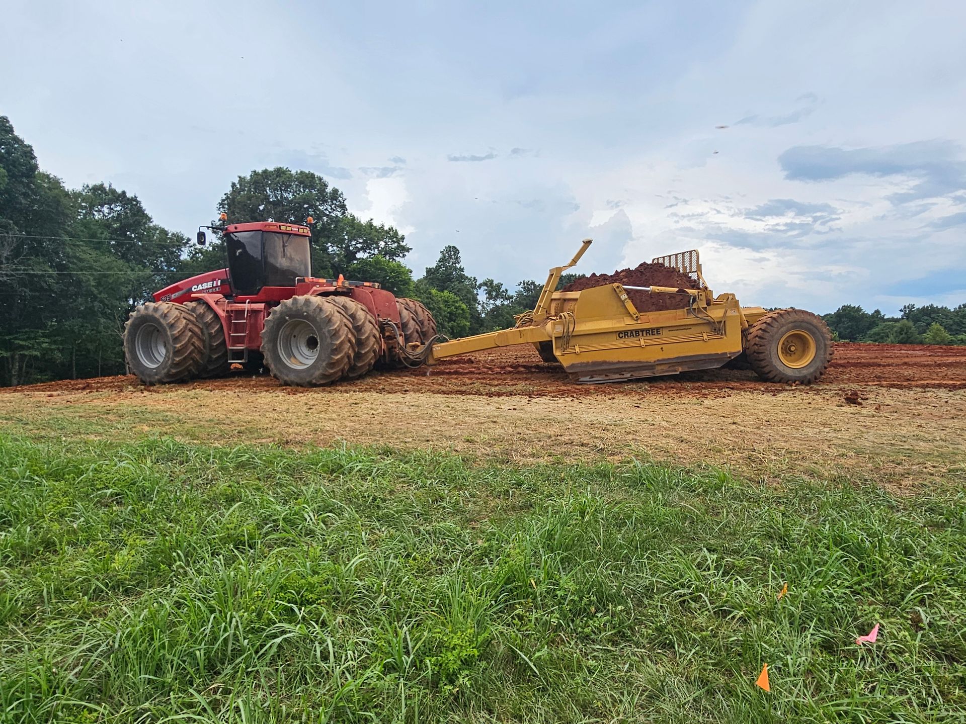 Two large agricultural machines, one red and one yellow, on a dirt field under a cloudy sky