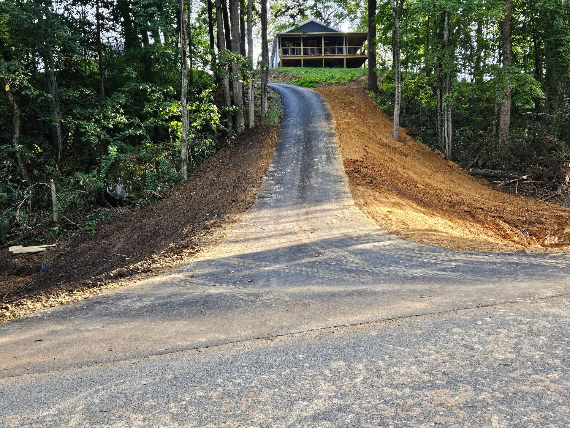 Steep paved driveway leading to a small cabin in a wooded forest.