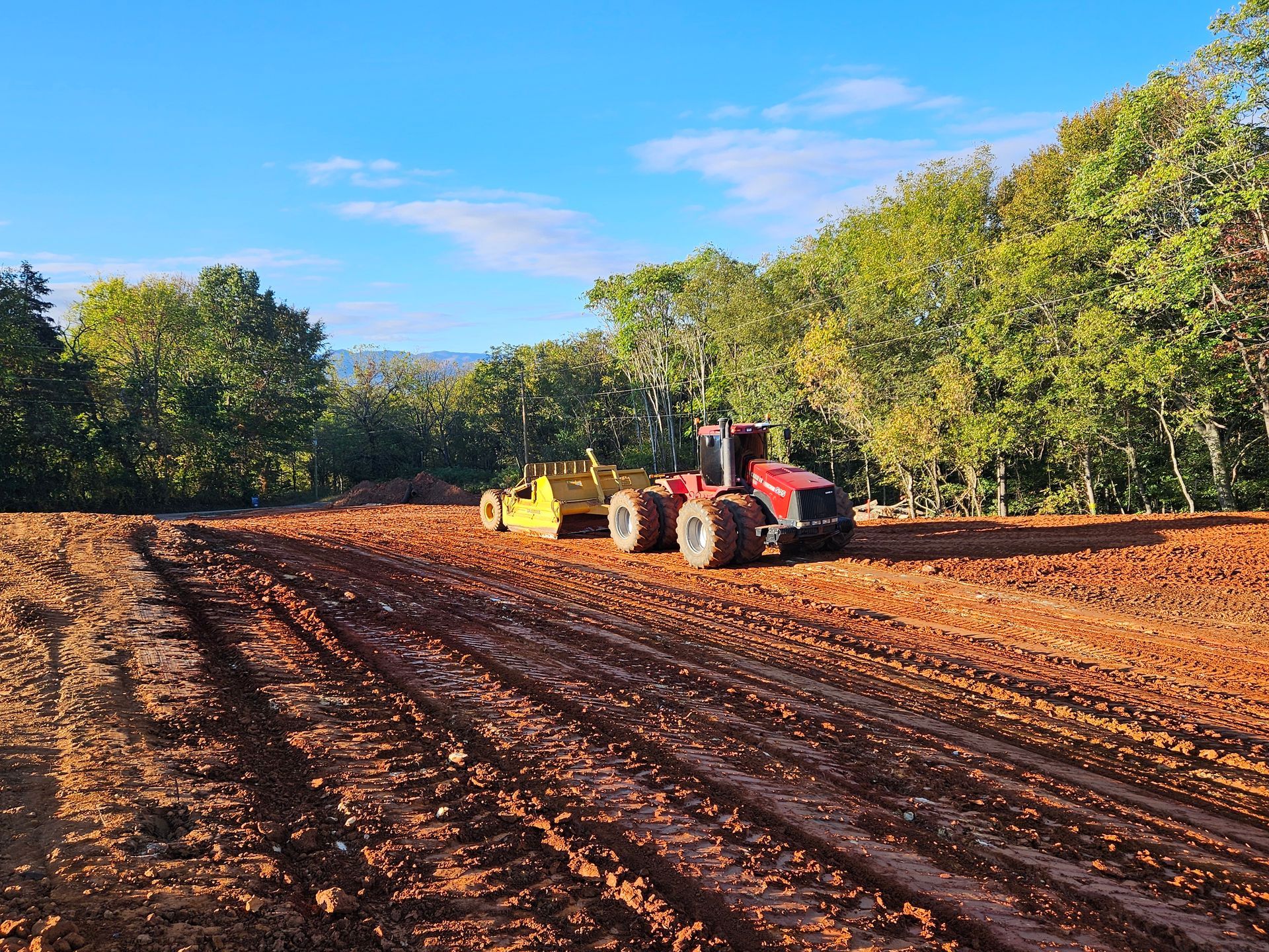 Red tractor plowing a brown field beside green trees under a blue sky