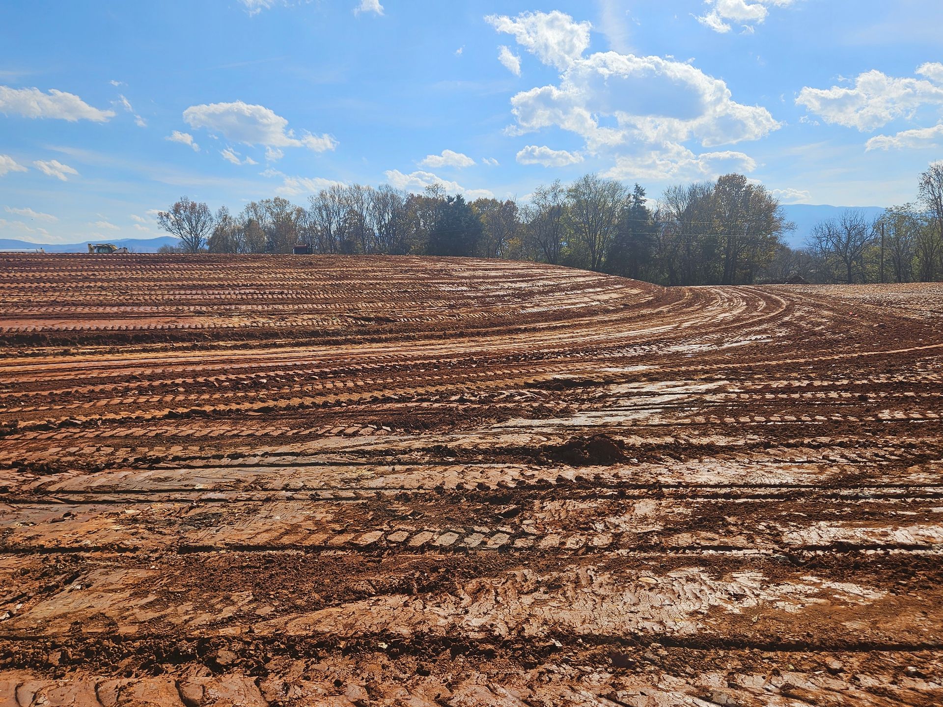 Plowed brown field under a blue sky with clouds and a line of trees in the distance