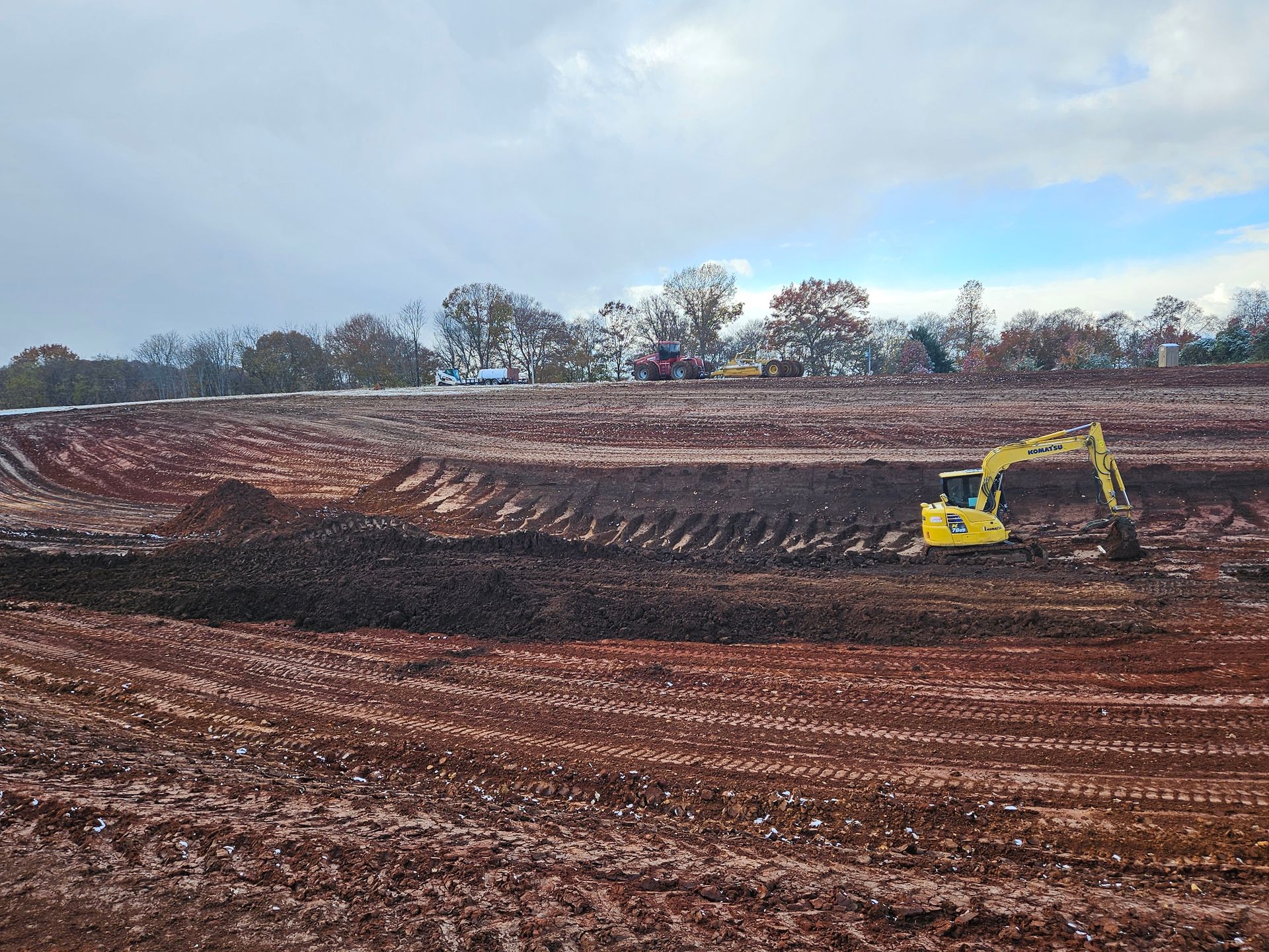 Yellow excavator on a muddy construction site under a cloudy sky