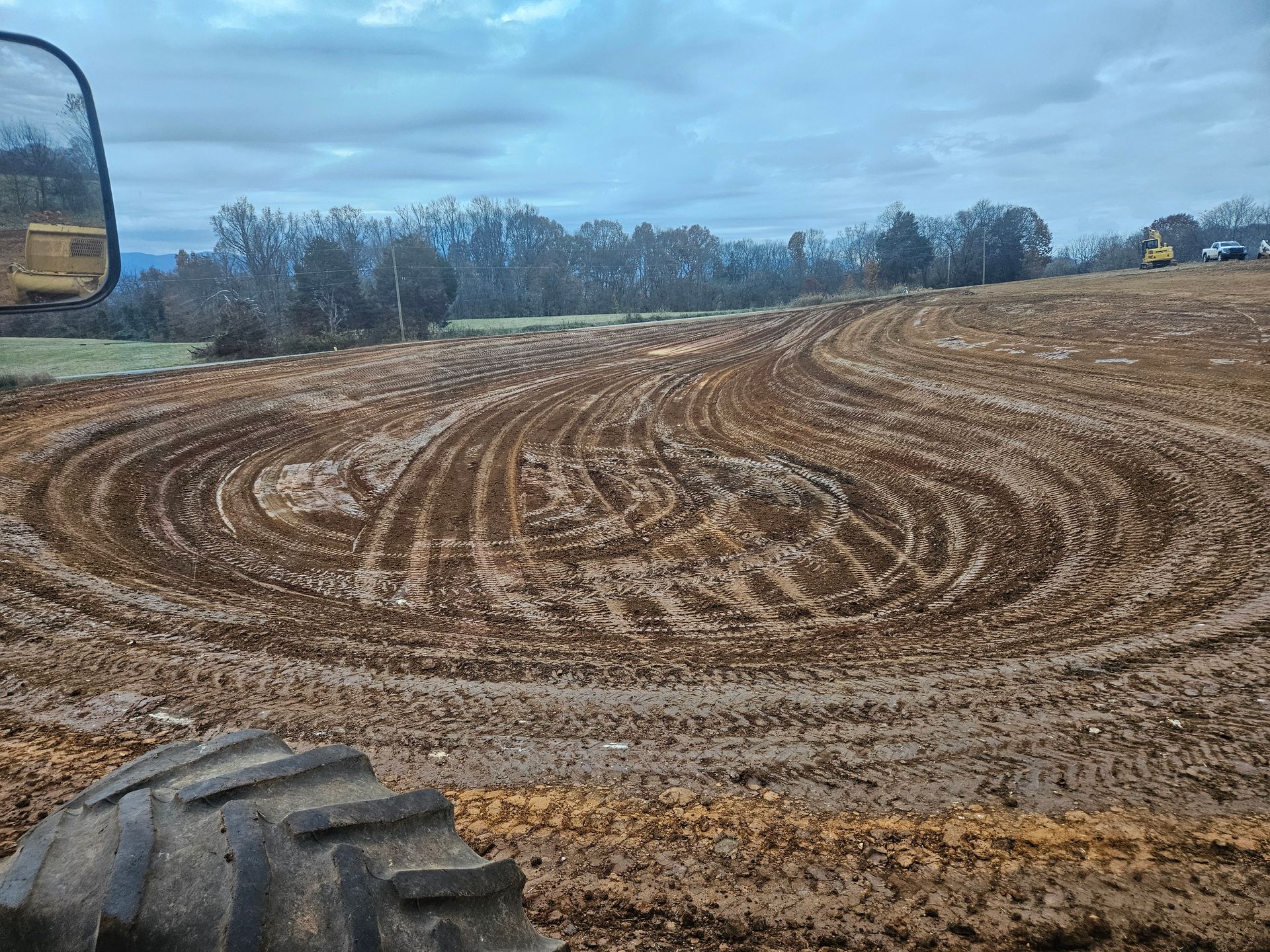 Freshly plowed muddy field with tractor tire tracks under a cloudy sky