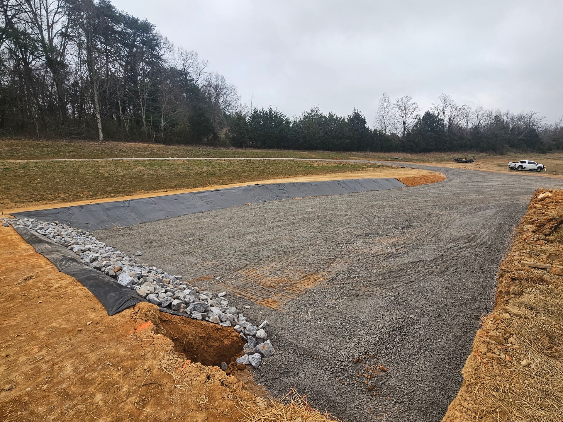 Gravel lot under construction with trees in the background and a white truck at the edge