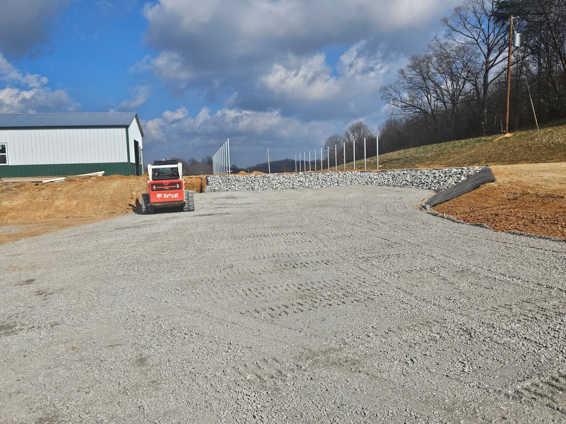 Gravel road under construction with a small red loader and retaining rocks on both sides