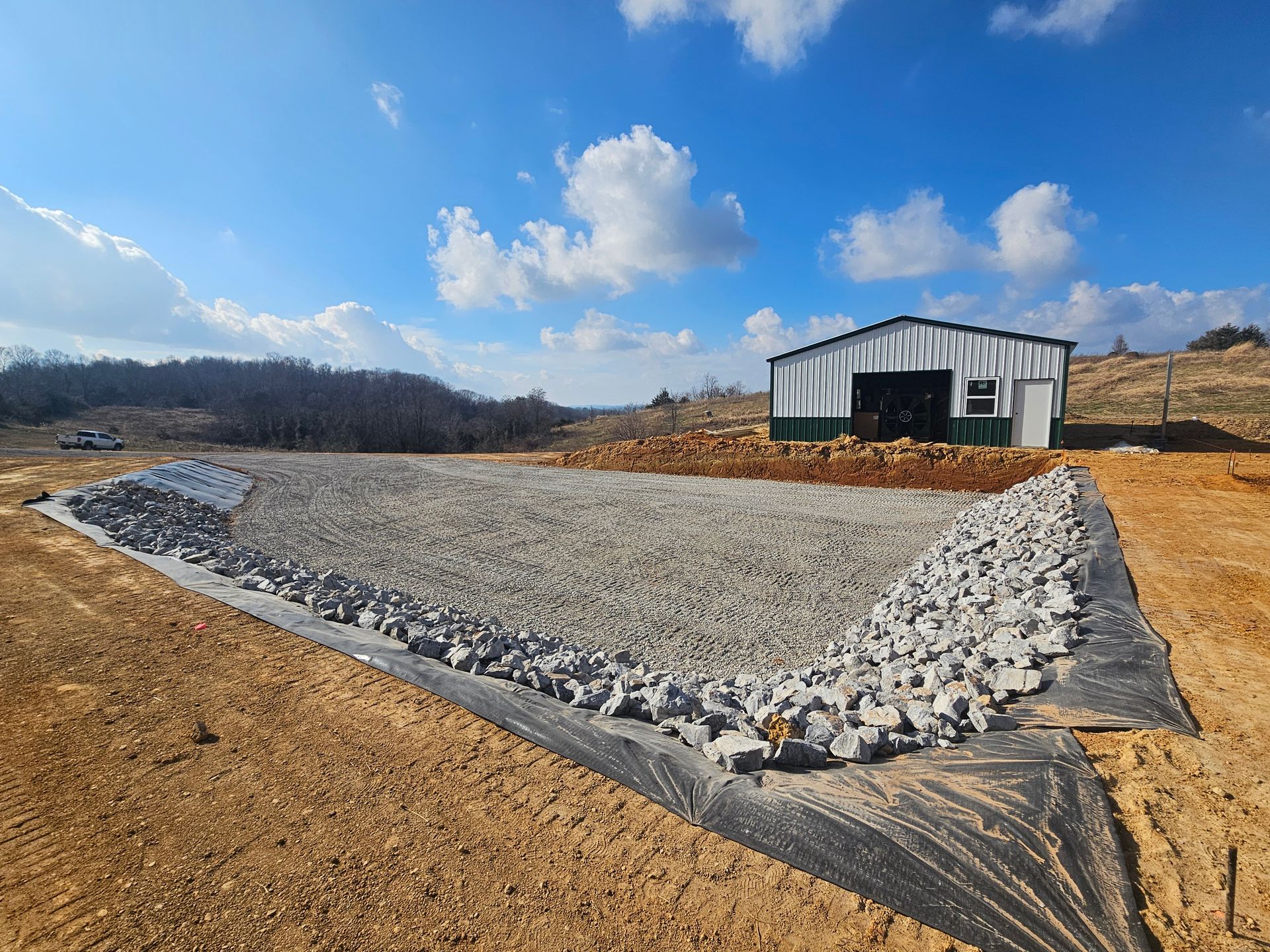 Gravel-lined drainage basin beside a metal shed under a blue sky with clouds