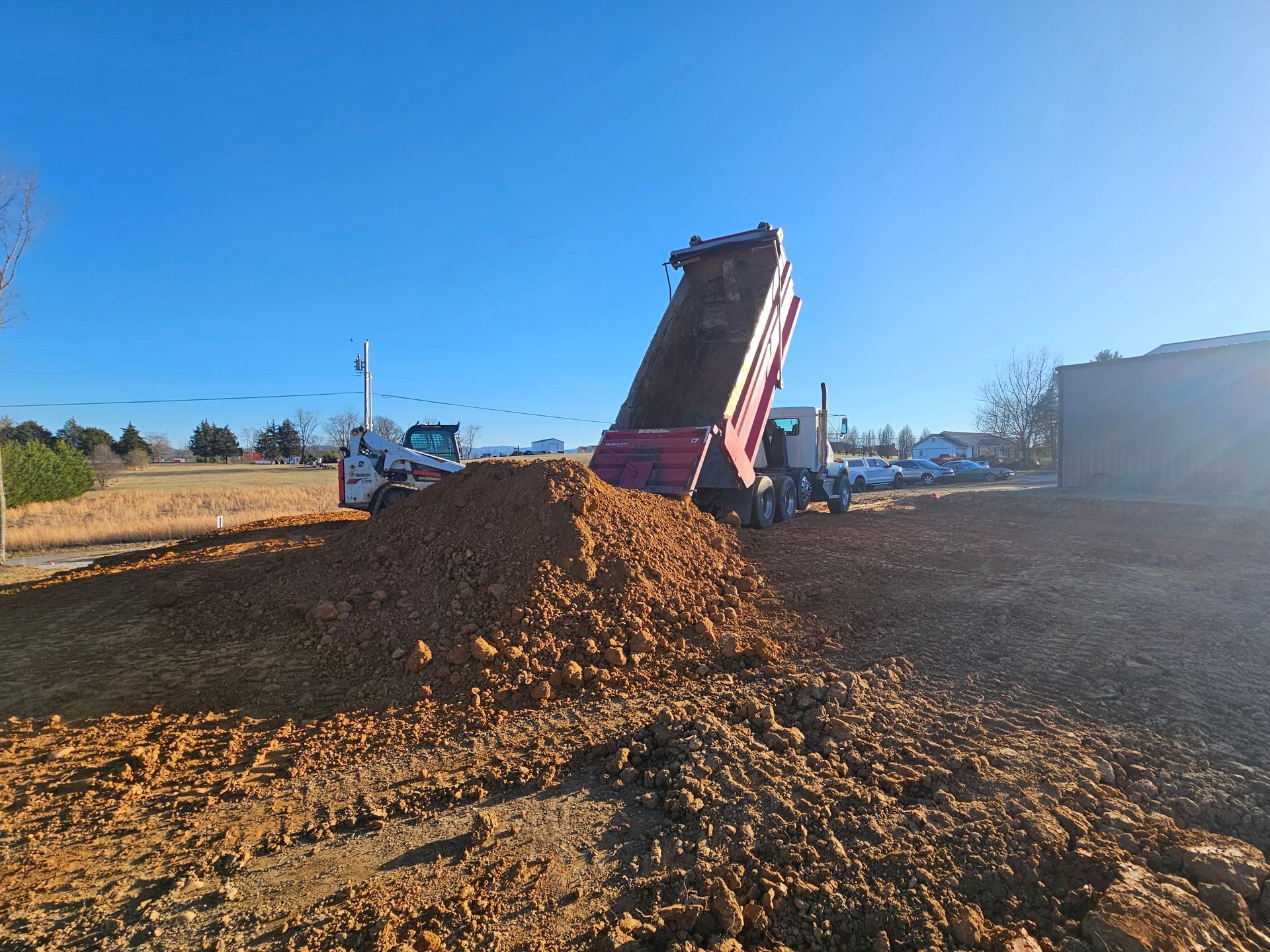 Construction site with dump truck unloading a pile of brown dirt under a clear blue sky
