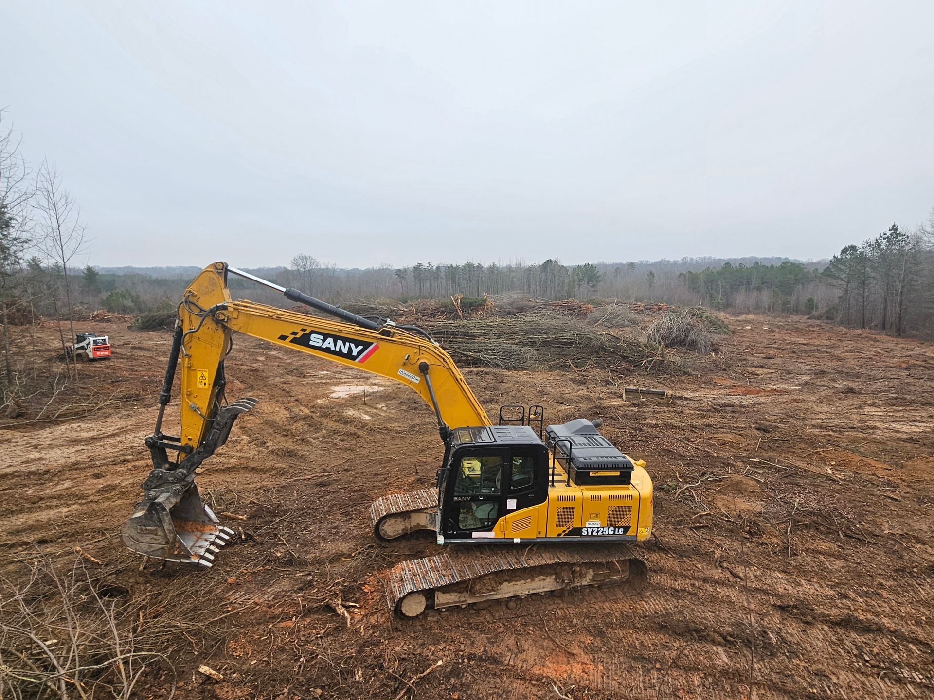 Yellow excavator clearing a logged hillside with bare trees in the background