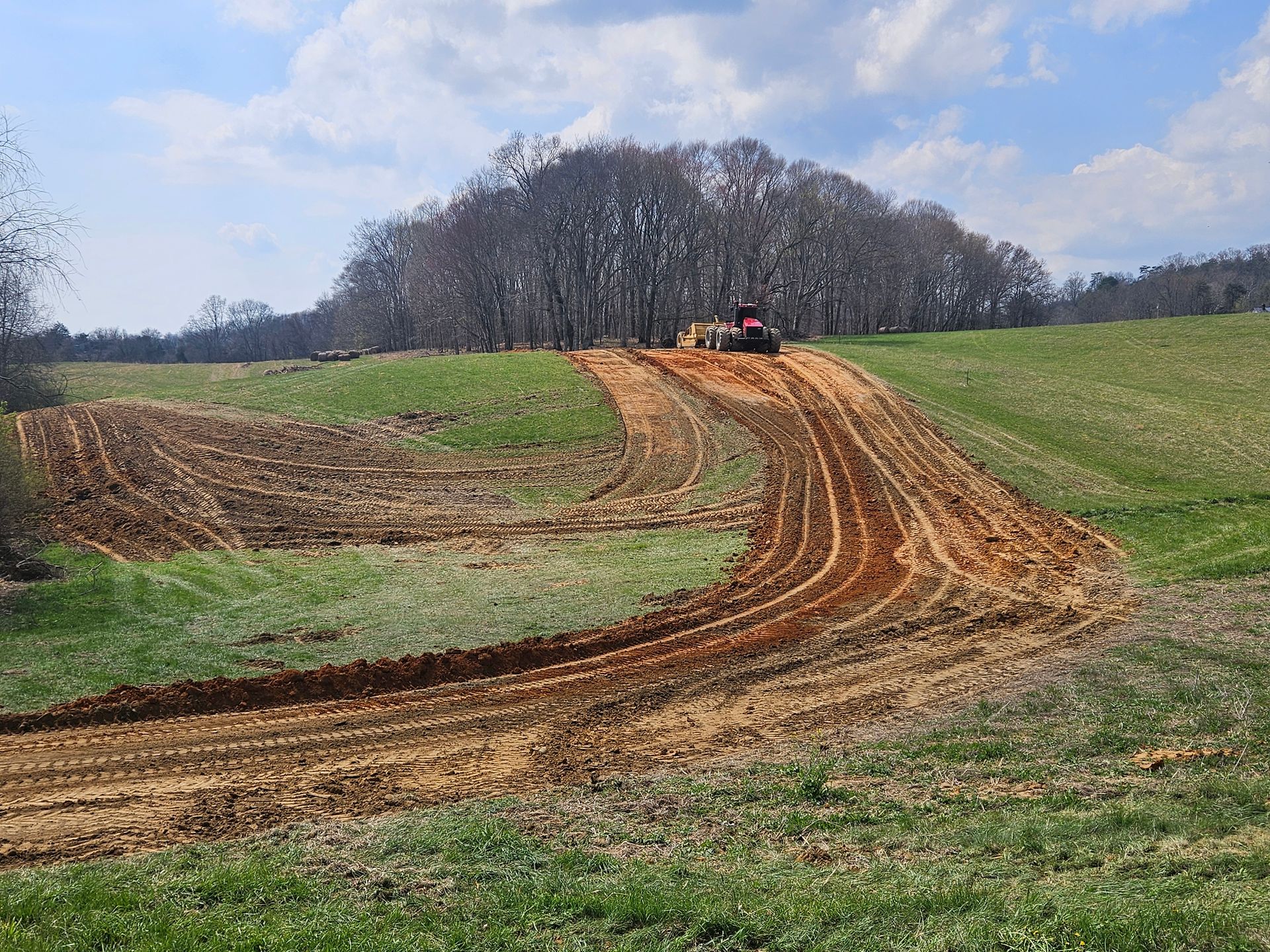 Tractor on muddy dirt track through green fields under a cloudy sky