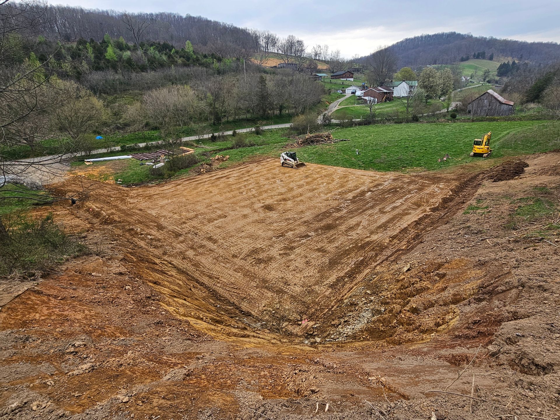 Freshly plowed brown field in a rural valley with green hills and a small yellow tractor in the distance