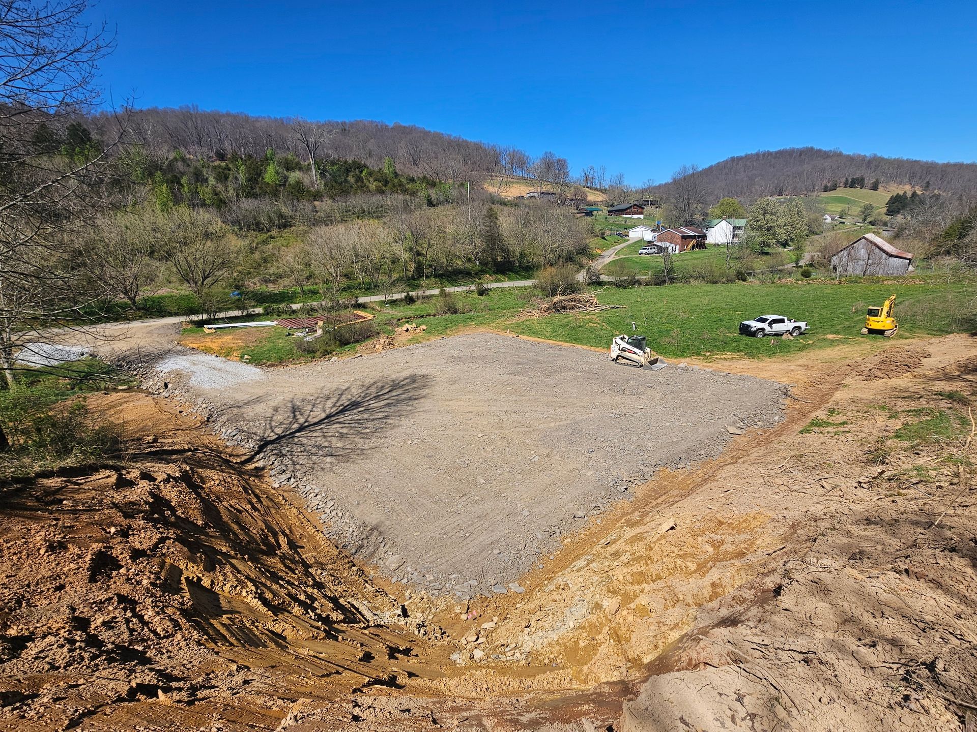 Gravel pit under construction in a rural valley with hills, trees, and a few houses in the background