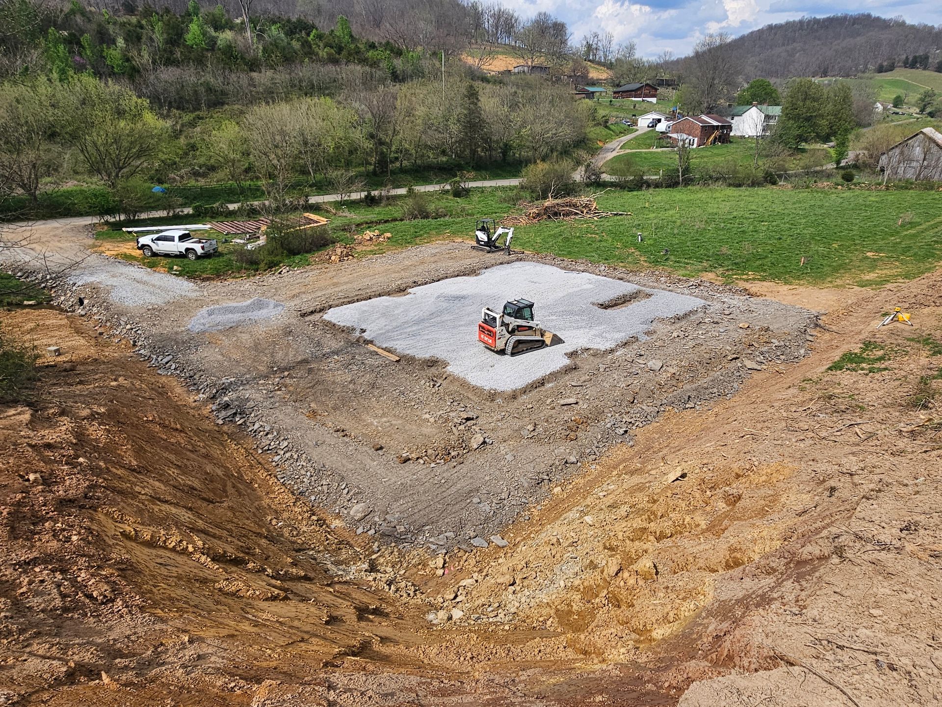 Excavation site with a concrete foundation pad in a rural hillside landscape, with a small machine on the slab.