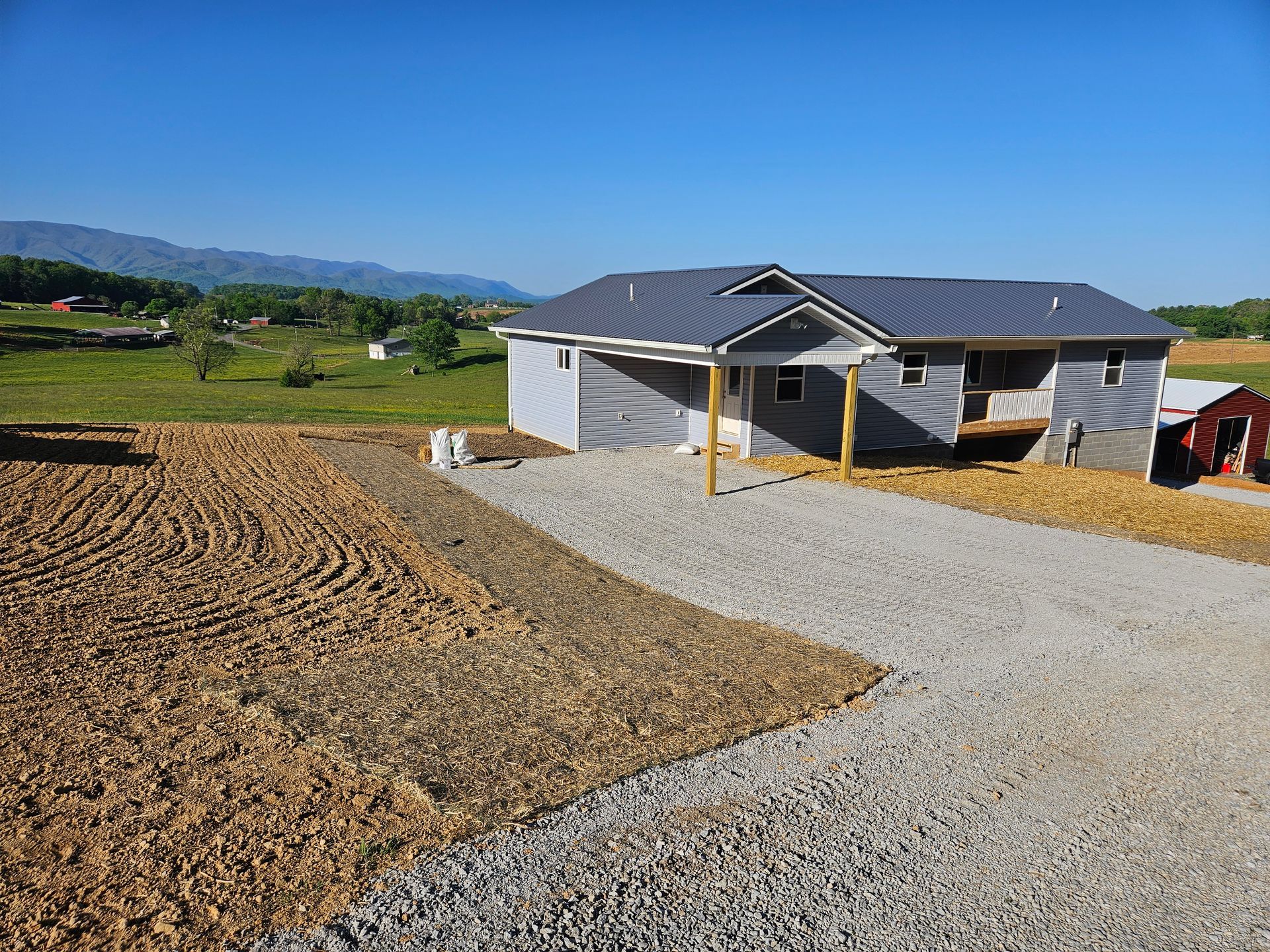 New house under construction beside a gravel driveway and tilled field in a rural landscape